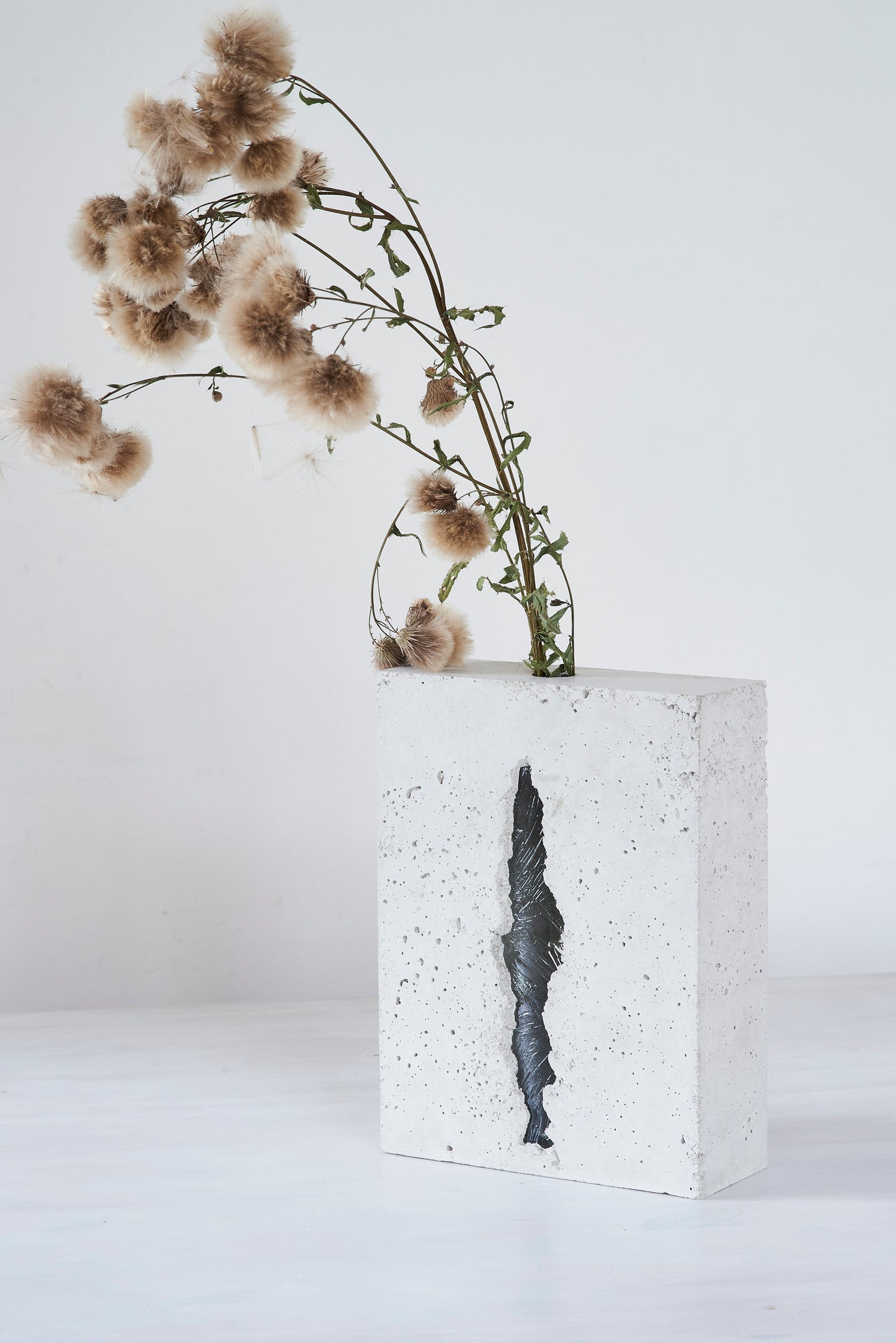 a vase made out of recycled glass and raw concrete set in white minimalistic interior on a table with decent flower.