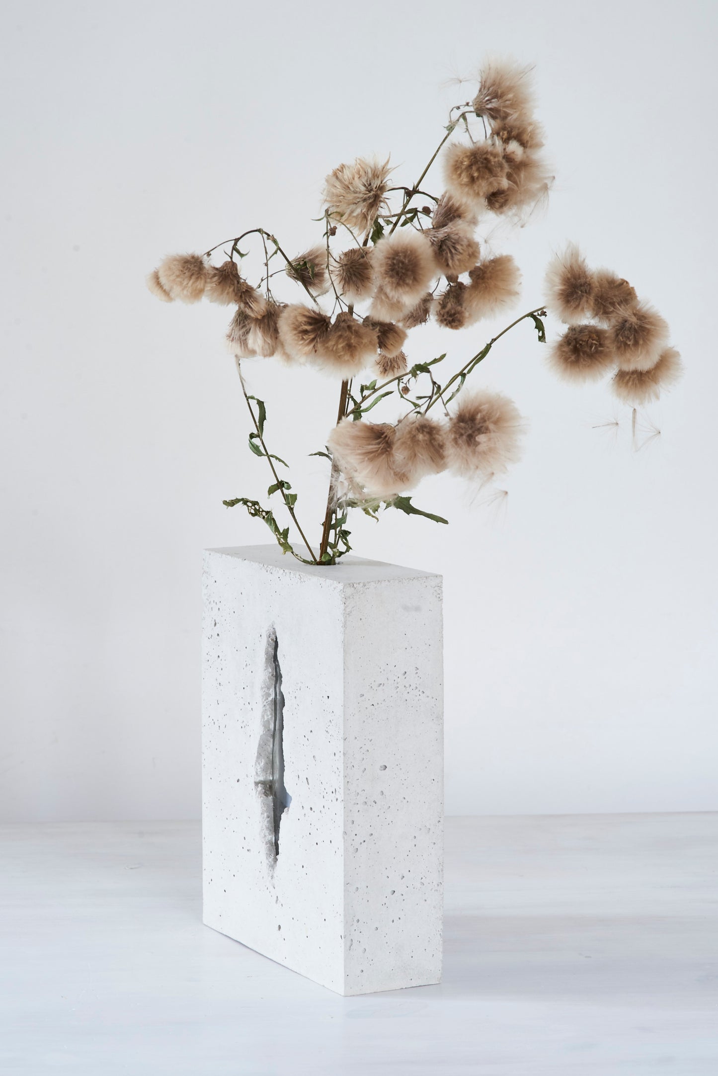 a vase made out of recycled glass and raw concrete set in white minimalistic interior on a table with decent flower.