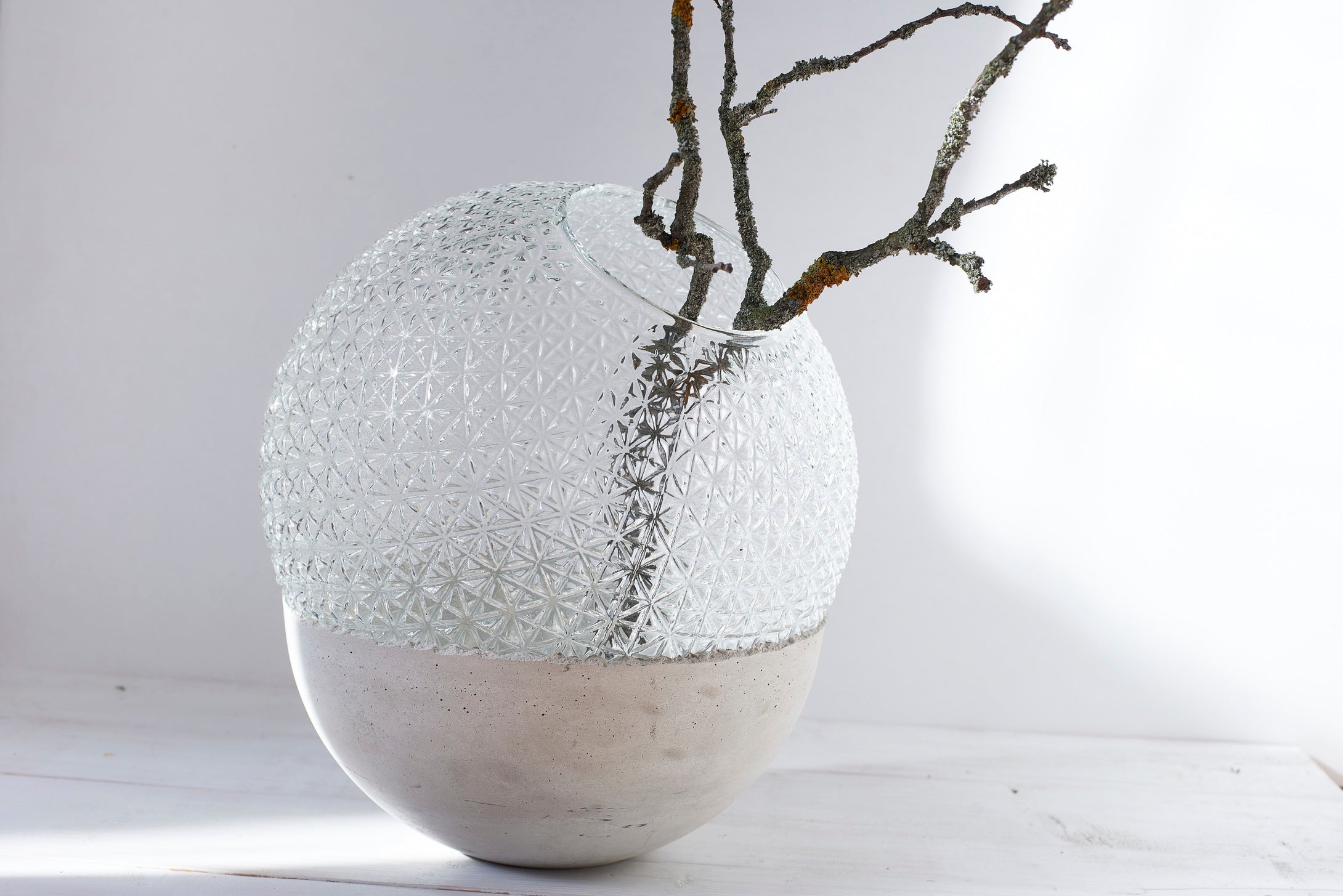 a large ball vase made out of recycled glass and raw concrete set in white minimalistic interior on a table with decent flower.