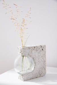 a vase made out of recycled glass and raw concrete set in white minimalistic interior on a table with decent flower.