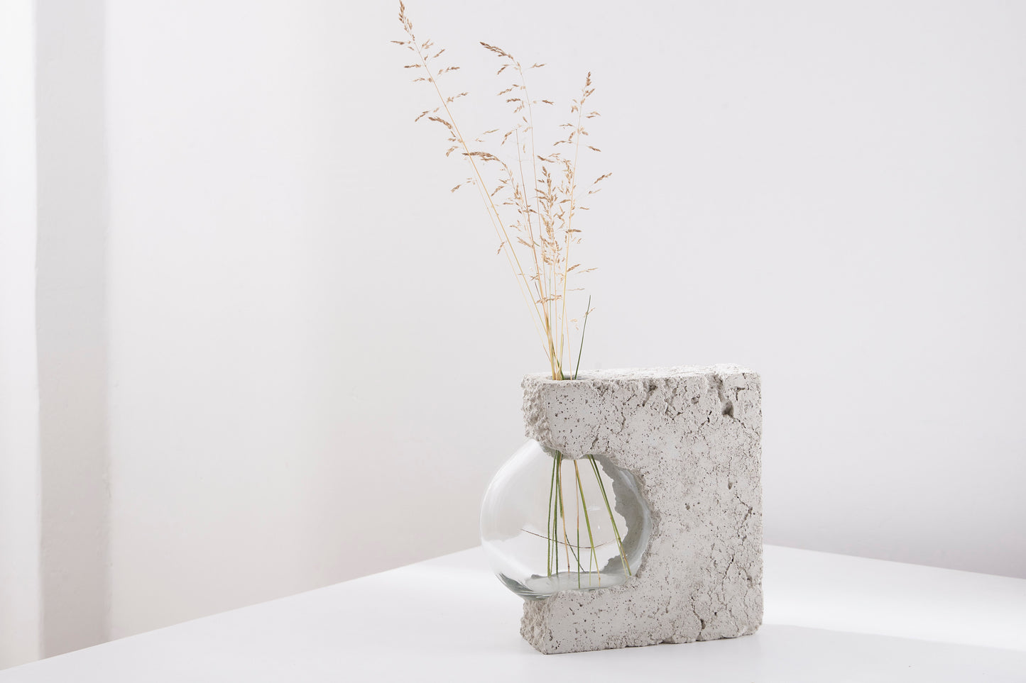 a vase made out of recycled glass and raw concrete set in white minimalistic interior on a table with decent flower.