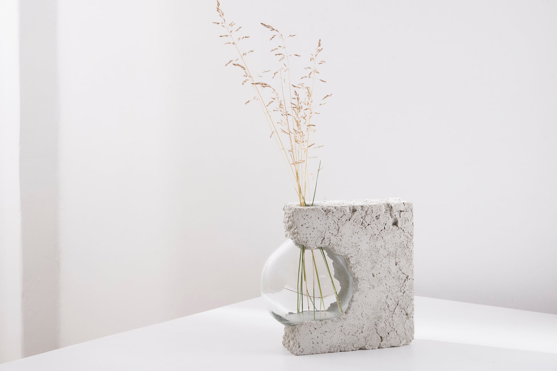 a vase made out of recycled glass and raw concrete set in white minimalistic interior on a table with decent flower.