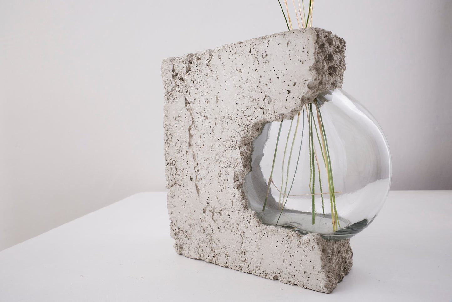 a vase made out of recycled glass and raw concrete set in white minimalistic interior on a table with decent flower.