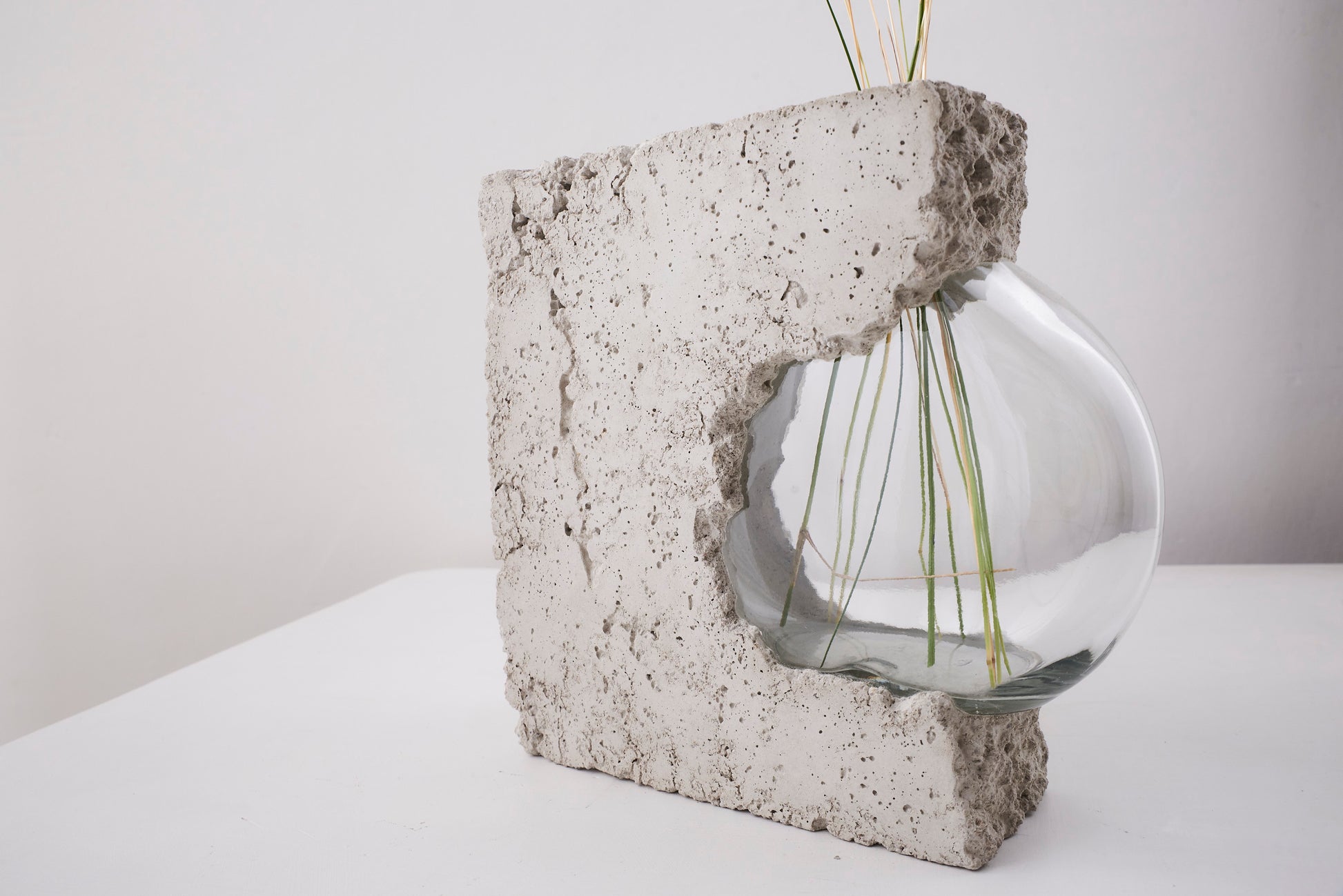 a vase made out of recycled glass and raw concrete set in white minimalistic interior on a table with decent flower.