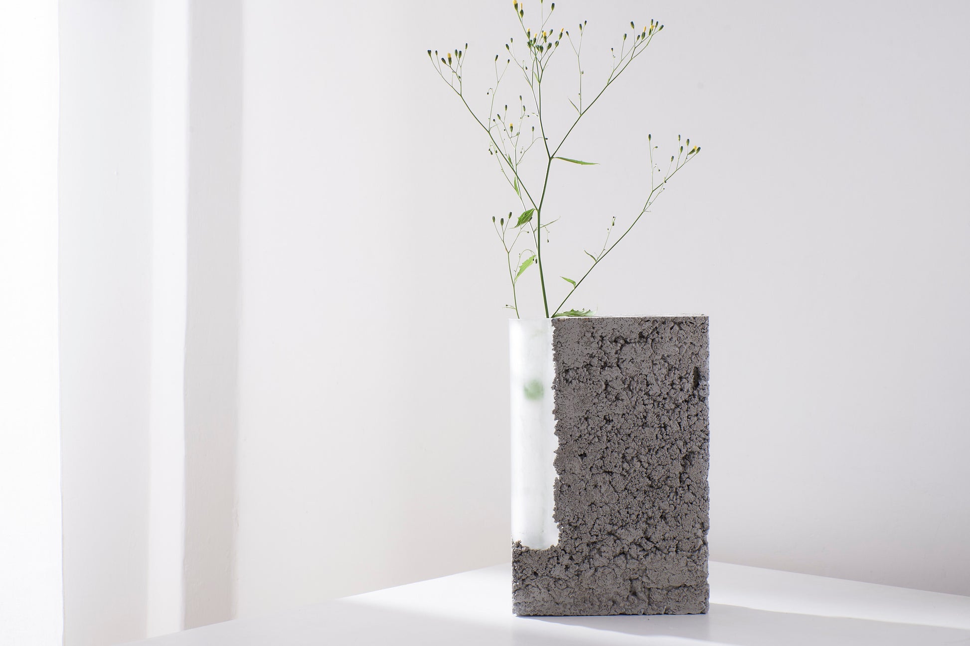 a vase made out of recycled glass and raw concrete set in white minimalistic interior on a table with decent flower. Art vase created by the Prague artist Petra Svejdarova a.k.a. Prasklo. Used materials are recycled glass and raw concrete without any plastificators.