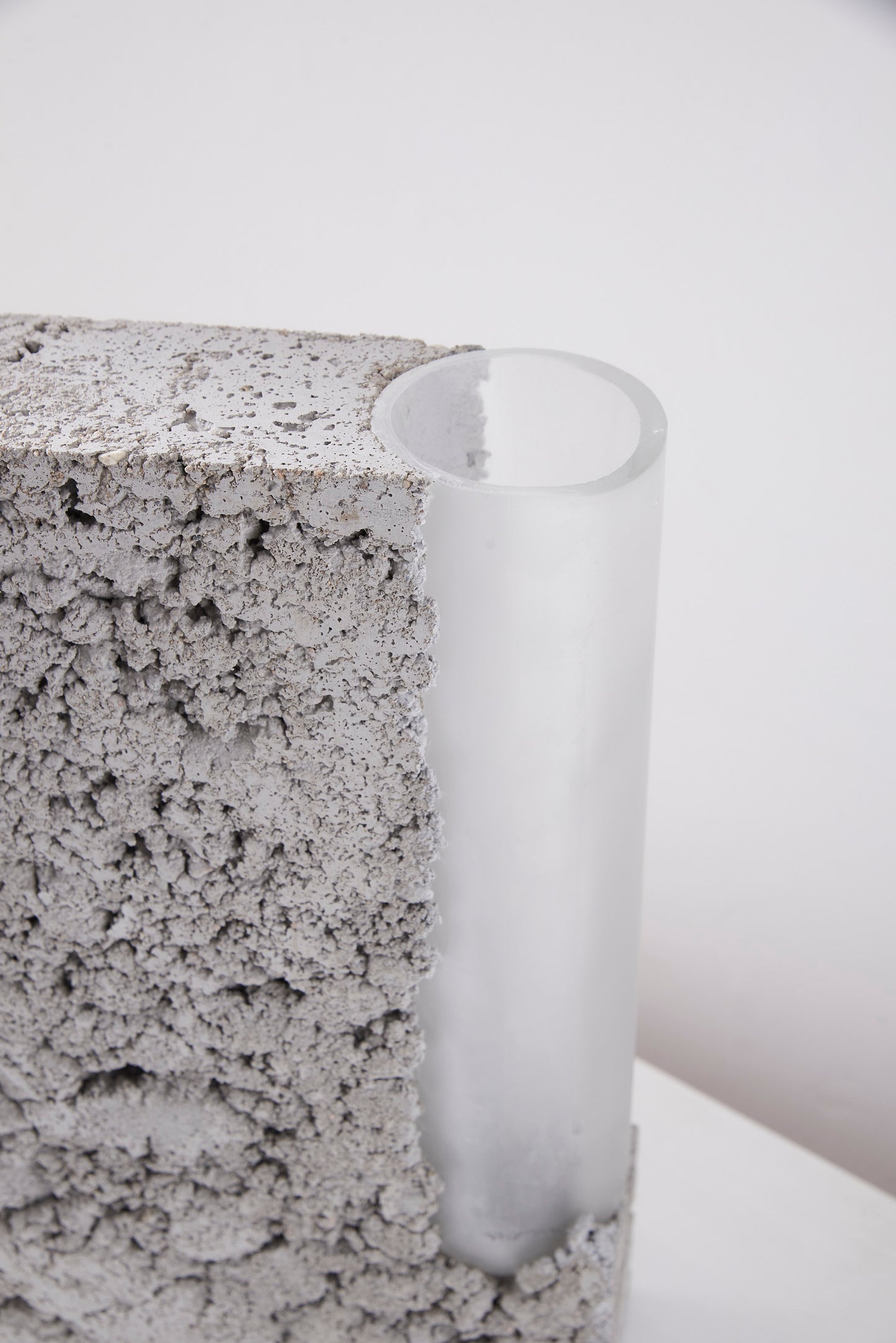 a vase made out of recycled glass and raw concrete set in white minimalistic interior on a table with decent flower.