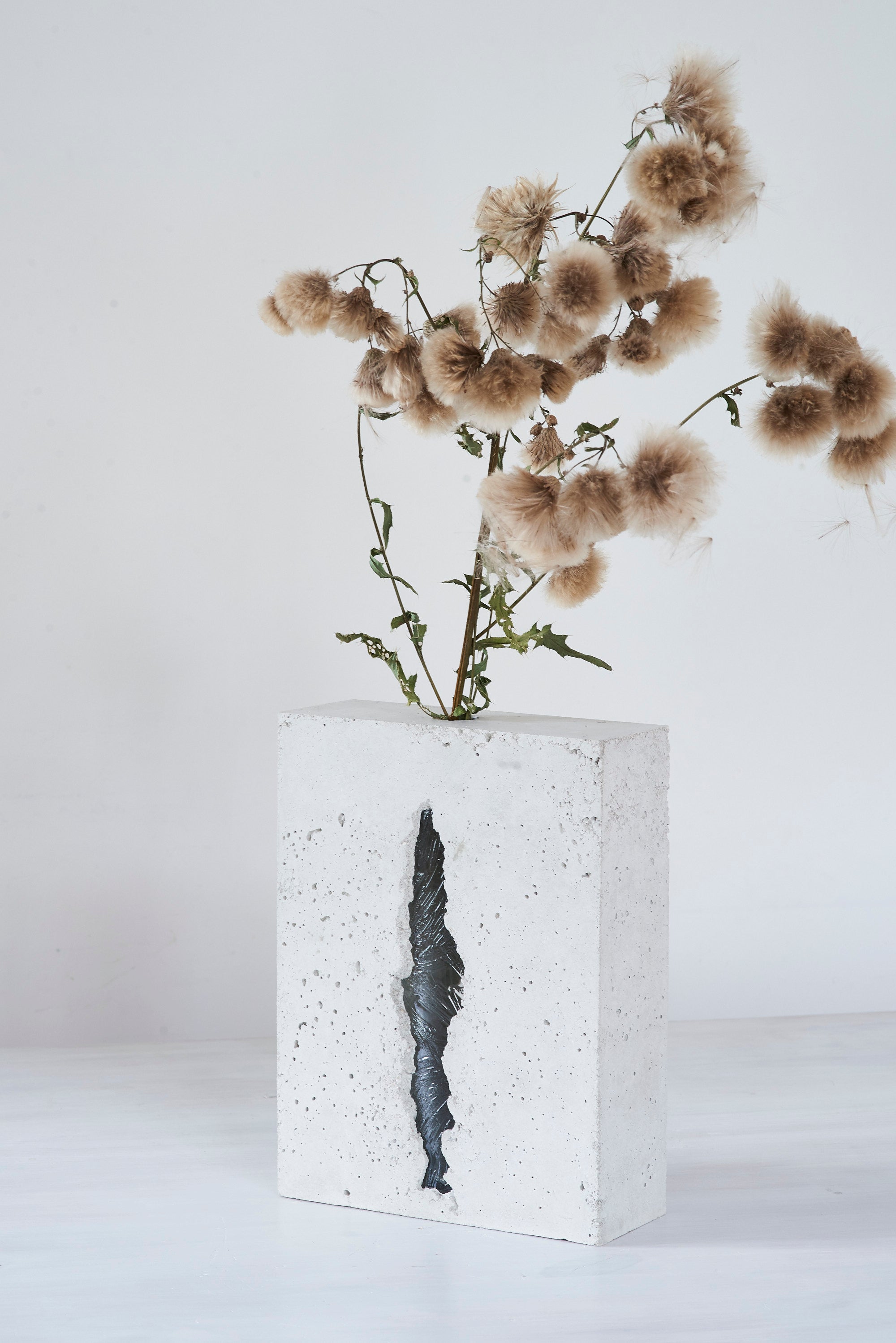 a vase made out of recycled glass and raw concrete set in white minimalistic interior on a table with decent flower.